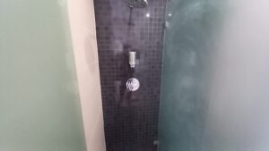 A modern shower area at 120 St Margaret's Road Twickenham boasts dark square tiles, a wall-mounted shower head, a soap dispenser, and a metallic faucet handle. Frosted glass panels on either side enhance its sleek, minimalistic look.