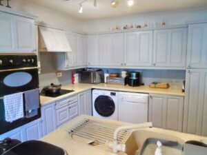 A clean, modern kitchen at 1 Boscombe Close Lincoln, featuring light-colored cabinets, a double oven, dishwasher, microwave, and washing machine. The countertops are clutter-free with a drying rack over the sink and small appliances like a toaster and coffee machine. On the market with Palace Auctions.