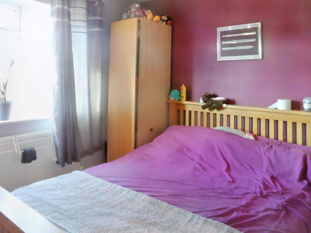 A bedroom at 1 Boscombe Close Lincoln features a wooden bed frame and a purple bedspread. A small stuffed animal rests on the bed. Next to it, a wooden wardrobe holds various stuffed animals on top. A framed picture adorns the purple wall, with light filtering through a partially open window. On the market with Palace Auctions.
