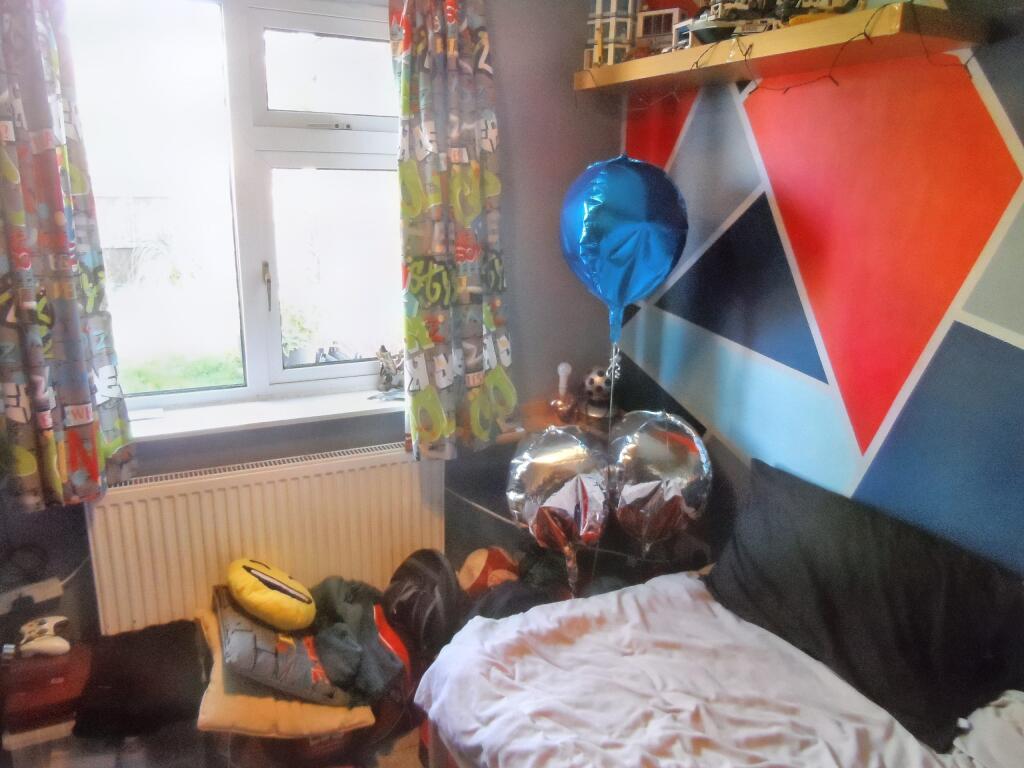 A bright and colorful bedroom at 1 Boscombe Close, Lincoln is on the market with Palace Auctions. It features a bed in the corner adorned with white bedding. Above the bed are geometric patterned walls. Balloons, one blue and the other silver, float nearby. Patterned curtains let in natural light while clothing is piled on the bed.