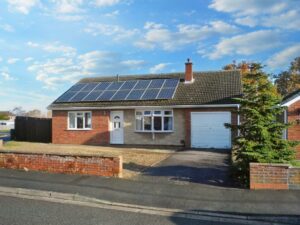 A one-story house at 1 Boscombe Close, Lincoln, featuring solar panels on the roof, a garage on the right, and a chimney. The facade is a combination of brick and beige siding. The front yard has minimal landscaping and a concrete driveway. The sky is clear with some clouds. On the market with Palace Auctions.