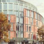 The future Harrods conneted hotel Modern building with a curved facade, featuring red brickwork and vertical white elements, surrounded by autumnal trees
