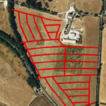 An aerial view of a rural area with fields and roads. A segment is highlighted with red lines, demarcating various plots. The plots are of different shapes and sizes, intersected by dirt roads. A few buildings are visible near the center-right of the image.