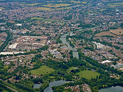 Property for sale Aerial view of a town with a river running through the center, surrounded by residential areas like 13 Maynard Court Rosefield Road Staines – upon – Thames TW18 4QD, green parks, trees, open fields, and visible buildings and roads throughout the landscape. Presented by Palace Auctions