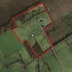 Aerial view of a large rural property outlined in red. The property includes several buildings and open, grassy fields bordered by trees and farmland. Surrounding areas are divided into different green fields with visible roads and paths.