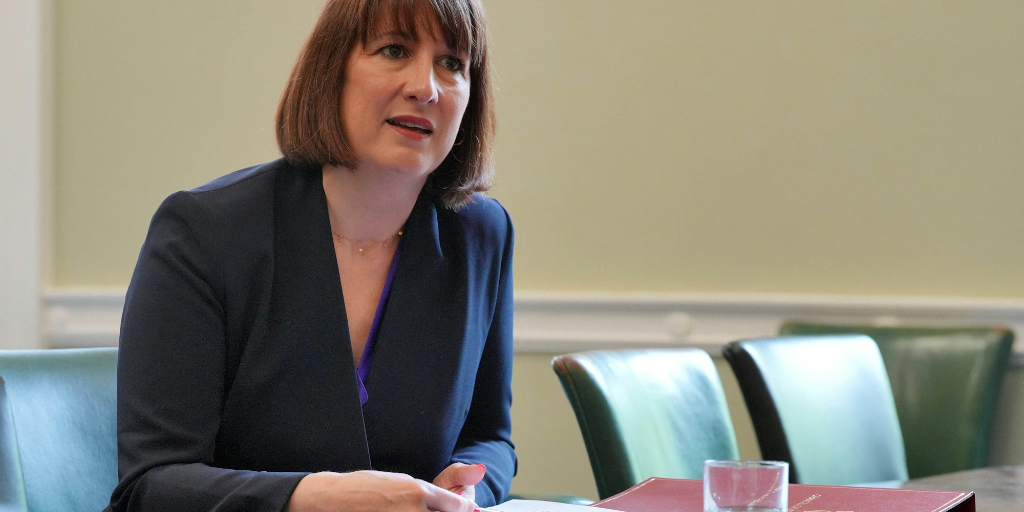 Property for sale by Auction Rachel Reeves, the Chancellor, with shoulder-length brown hair, sits at a conference table with a red folder open in front of her. She is wearing a dark blazer and a blue top. Two green chairs are visible in the background. She appears to be speaking or presenting something. Presented by Palace Auctions