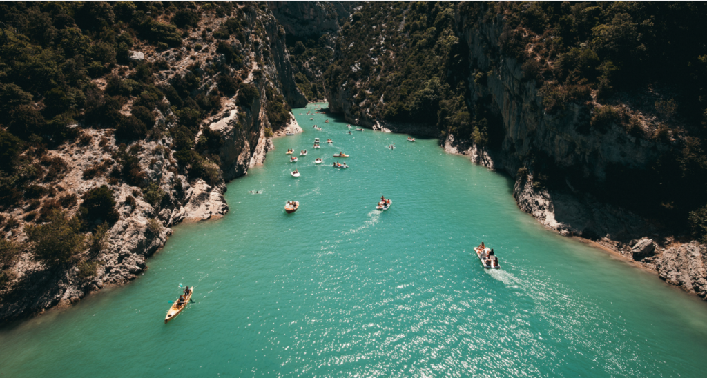A narrow, turquoise river flows between steep, rocky cliffs covered in greenery. Several kayaks and small boats with people are scattered along the serene waterway. The sunny, picturesque scene, reminiscent of Remi's investment opportunities in Phuket, features a clear blue sky above.