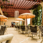 A spacious outdoor dining area with several tables and chairs under large beige umbrellas. A pergola with greenery and hanging decorations provides partial shade. The serene setting is ideal for relaxed dining at the Grand Pacific Sovereign Resort & Spa, an off-market hotel investment opportunity.