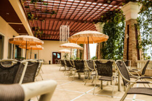 A spacious outdoor dining area with several tables and chairs under large beige umbrellas. A pergola with greenery and hanging decorations provides partial shade. The serene setting is ideal for relaxed dining at the Grand Pacific Sovereign Resort & Spa, an off-market hotel investment opportunity.