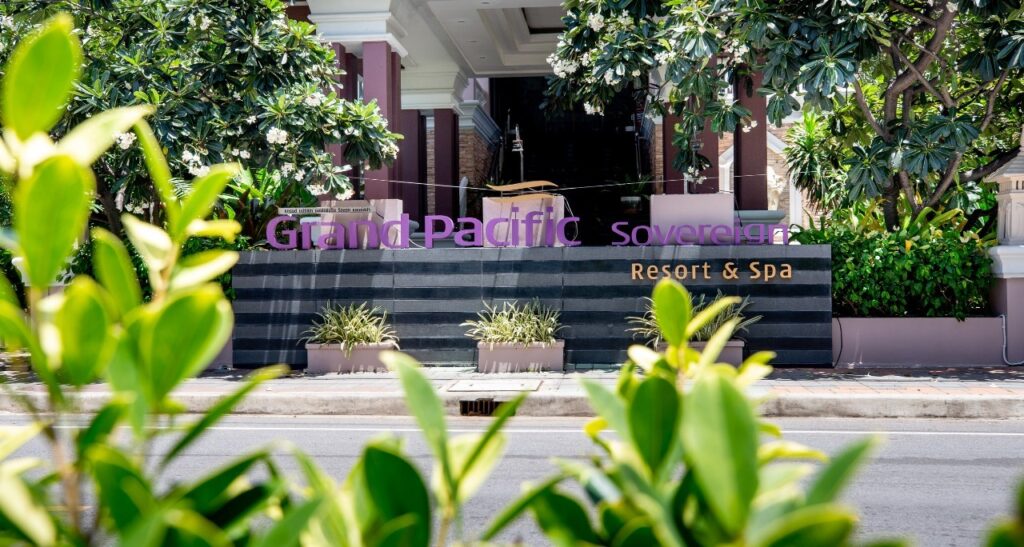Entrance sign of the "Grand Pacific Sovereign Resort & Spa" with vibrant greenery in the foreground. The illuminated sign, set against a backdrop of lush trees and architectural details, highlights this off market hotel investment opportunity.