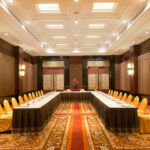 A spacious, well-lit conference room at the Grand Pacific Sovereign Resort & Spa features an elegant U-shaped table setup. The black and gold tablecloth is surrounded by yellow-gold chairs. With warm lighting, paneled walls, intricate decor, and a patterned carpet, it's the perfect off-market hotel investment opportunity.