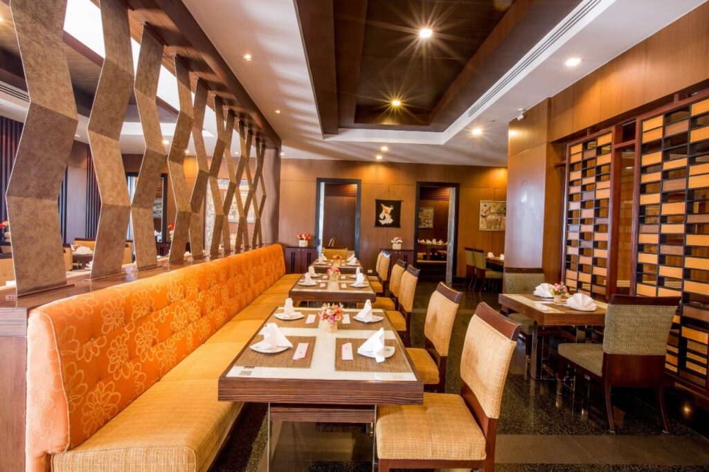 Modern restaurant interior with wooden accents at the Grand Pacific Sovereign Resort & Spa, featuring orange cushioned seating, neatly arranged tables set with white napkins, and elegant lighting. The area has a warm, inviting atmosphere with decorative elements and framed artwork on the walls.