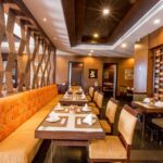 Modern restaurant interior with wooden accents at the Grand Pacific Sovereign Resort & Spa, featuring orange cushioned seating, neatly arranged tables set with white napkins, and elegant lighting. The area has a warm, inviting atmosphere with decorative elements and framed artwork on the walls.