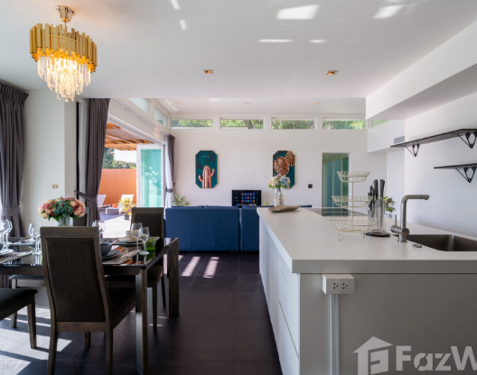 Modern open-plan living space with a dining table set for four, a white kitchen island, and a blue sofa in the background. Large windows and sliding doors allow natural light to fill the room. Shelves and wall art add to the contemporary decor.