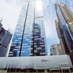 A modern urban scene featuring a high-rise building with a "Citibank" logo at the bottom. Flanked by other skyscrapers under construction, the blue sky with scattered clouds forms a backdrop. The main building, ideal for office investment business for sale in Singapore, has a sleek glass facade with geometric patterns.