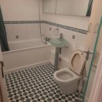 Property for sale by Auction A bathroom featuring a bathtub with a showerhead, a green pedestal sink, a toilet with the lid open, and a floor with black and white checkered tiles. The walls are white with decorative blue and white tiles lining the middle. A large mirror is above the sink and tub. Presented by Palace Auctions