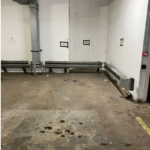 Property for sale by Auction An empty parking space in an indoor parking garage. The ground is concrete with some dark stains and the number "33" is painted in white. The walls are white with some exposed pipes and electrical wiring. Fluorescent lights are visible on the ceiling. Presented by Palace Auctions
