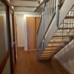 Property for sale by Auction A hallway with wooden flooring and white walls features a modern staircase with metallic railings and wooden steps on the right. On the left side, there are glass doors with wooden frames. A wooden ceiling adds warmth to the space. Presented by Palace Auctions