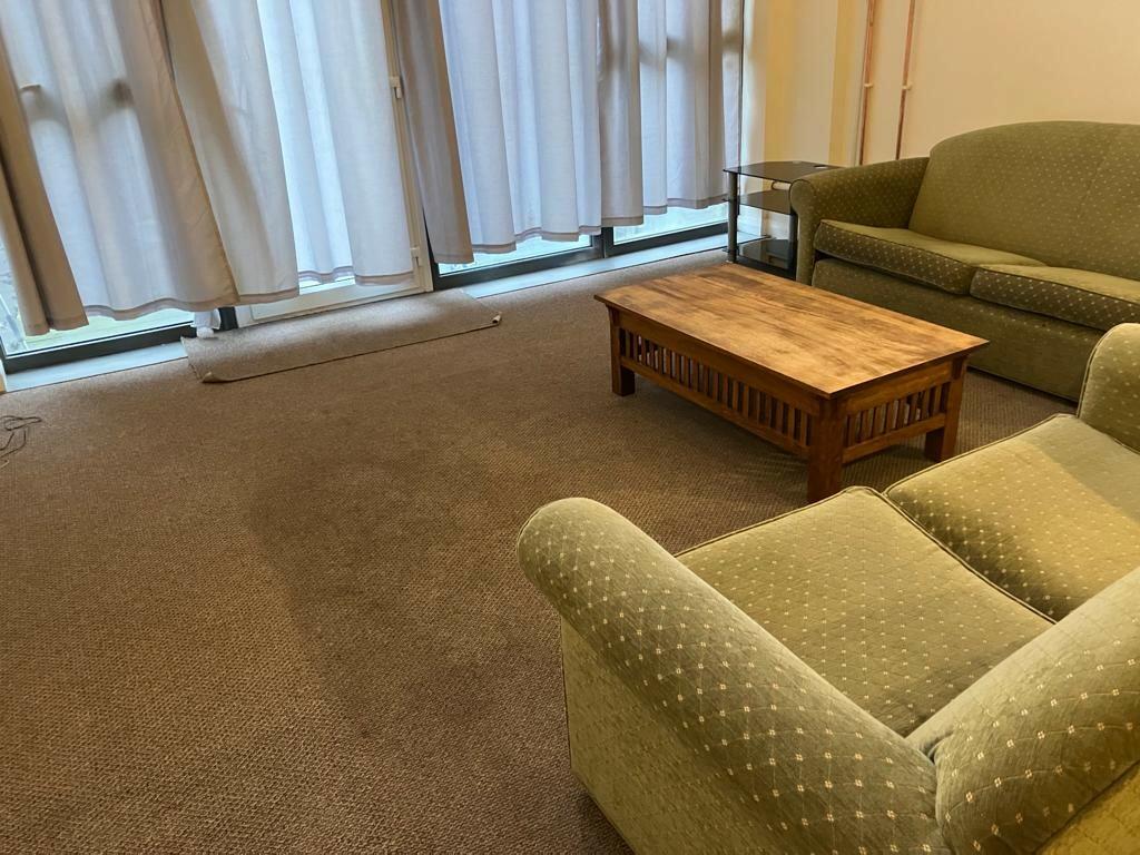 Property for sale by Auction A living room with a green couch and matching armchair, both with polka dot upholstery, placed on a carpeted floor. There's a wooden coffee table in front of the couch. The room has large windows with closed white curtains and a glass side table beside the couch. Presented by Palace Auctions