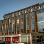 Property for sale by Auction A modern six-story commercial building with large windows and a brown brick facade. The ground floor features a store with large red sale signs in the windows, advertising a 70% discount. Nearby, a Nottingham apartment for sale by auction adds to the area's dynamic real estate offerings. Presented by Palace Auctions
