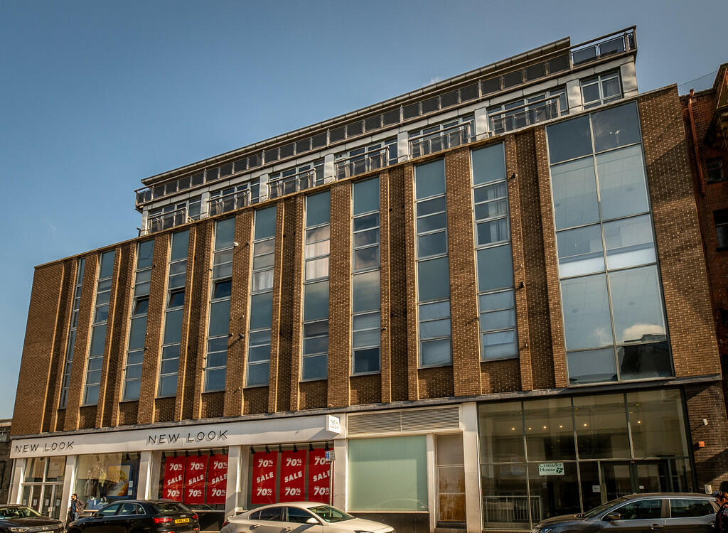 Property for sale by Auction A modern six-story commercial building with large windows and a brown brick facade. The ground floor features a store with large red sale signs in the windows, advertising a 70% discount. Nearby, a Nottingham apartment for sale by auction adds to the area's dynamic real estate offerings. Presented by Palace Auctions