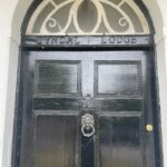 Property for sale by Auction A black wooden door with an ornate circular knocker at the center and the number 79 above it. An arched window with white trim is above the door, and "Tyndal Lodge" is inscribed above the door in the wooden frame. Presented by Palace Auctions
