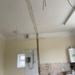 Property for sale by Auction A room under renovation, with an exposed shower unit and pipes on the wall. The ceiling has visible, unfinished seams and hanging wires. The wall has peeled paint and plaster, and construction materials are scattered on the floor. There's a toilet without a seat. Presented by Palace Auctions