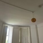 Property for sale by Auction A room with white walls and a high ceiling featuring a dome-shaped light fixture hanging down. Two tall windows with wooden shutters are partially opened, allowing some natural light to enter. The room has a clean and minimalistic appearance. Presented by Palace Auctions