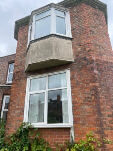 Property for sale by Auction A two-story brick house with a protruding bay window on the upper floor and a standard window on the ground level. The bay window has a concrete base. There is some greenery adjacent to the building, and neighboring structures are visible in the background. Presented by Palace Auctions