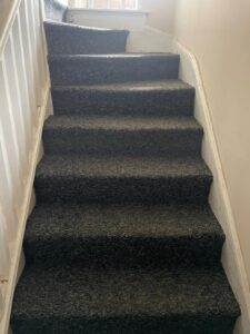 Property for sale by Auction A set of steep, carpeted stairs with dark-gray carpeting, white walls, and a white wooden railing on the left side. The staircase curves slightly to the left at the top. Presented by Palace Auctions