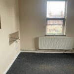 Property for sale by Auction An empty room with beige walls and a grey carpet. A window with closed blinds is on one wall above a white radiator. There are a few wall fixtures and an open cable dangling from the wall. Presented by Palace Auctions