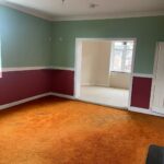 Property for sale by Auction A partially furnished room with green and red walls, an orange carpet, and a white door. An adjacent room with white walls and a beige carpet is visible through a large open doorway. Natural light shines through the windows in both rooms. Presented by Palace Auctions
