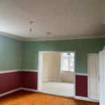 Property for sale by Auction An empty room with green and burgundy walls, white trim, and orange carpet. There is a doorway leading to an adjoining room with white walls and light-colored carpet. A window in the far room allows natural light to enter. Light fixtures hang from the ceilings. Presented by Palace Auctions