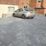 Property for sale by Auction A grey car is parked on a freshly laid brick driveway in front of a multi-level brick house. The house has a beige ground floor and traditional red bricks on the upper levels. Several windows are visible, and the driveway appears newly constructed. Presented by Palace Auctions