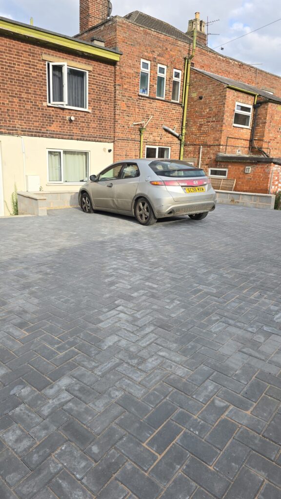 Property for sale by Auction A grey car is parked on a freshly laid brick driveway in front of a multi-level brick house. The house has a beige ground floor and traditional red bricks on the upper levels. Several windows are visible, and the driveway appears newly constructed. Presented by Palace Auctions