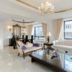 Property for sale by Auction A spacious, elegant living room features a chandelier, floor-length curtains, and large windows that let in ample light. The room boasts modern and classic furniture, including a white sofa, a loveseat, and a dark wooden coffee table with a decorative centerpiece. Presented by Palace Auctions