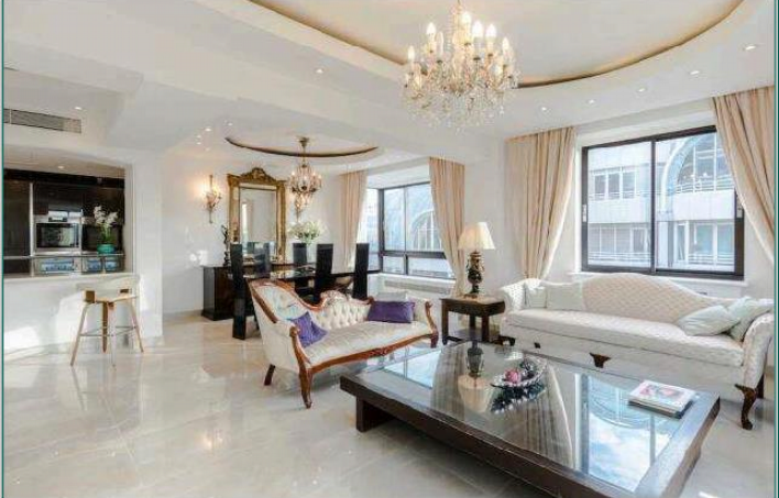 Property for sale by Auction A spacious, elegant living room features a chandelier, floor-length curtains, and large windows that let in ample light. The room boasts modern and classic furniture, including a white sofa, a loveseat, and a dark wooden coffee table with a decorative centerpiece. Presented by Palace Auctions