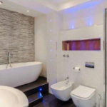 Property for sale by Auction Modern bathroom with a freestanding white bathtub against a tiled wall, a sleek glass-enclosed shower, and a toilet next to a bidet. Ambient blue lighting accents the clean, minimalist design. White fixtures and fittings complement the contemporary aesthetic. Presented by Palace Auctions