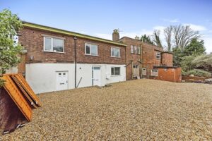 Property for sale by Auction A substantial residential and development opportunity awaits in this large brick building with a gravel courtyard. Featuring multiple doors and windows on the ground floor, the site includes wooden boards propped against a wall on the left. Trees and bushes are visible in the background under a clear sky. Presented by Palace Auctions
