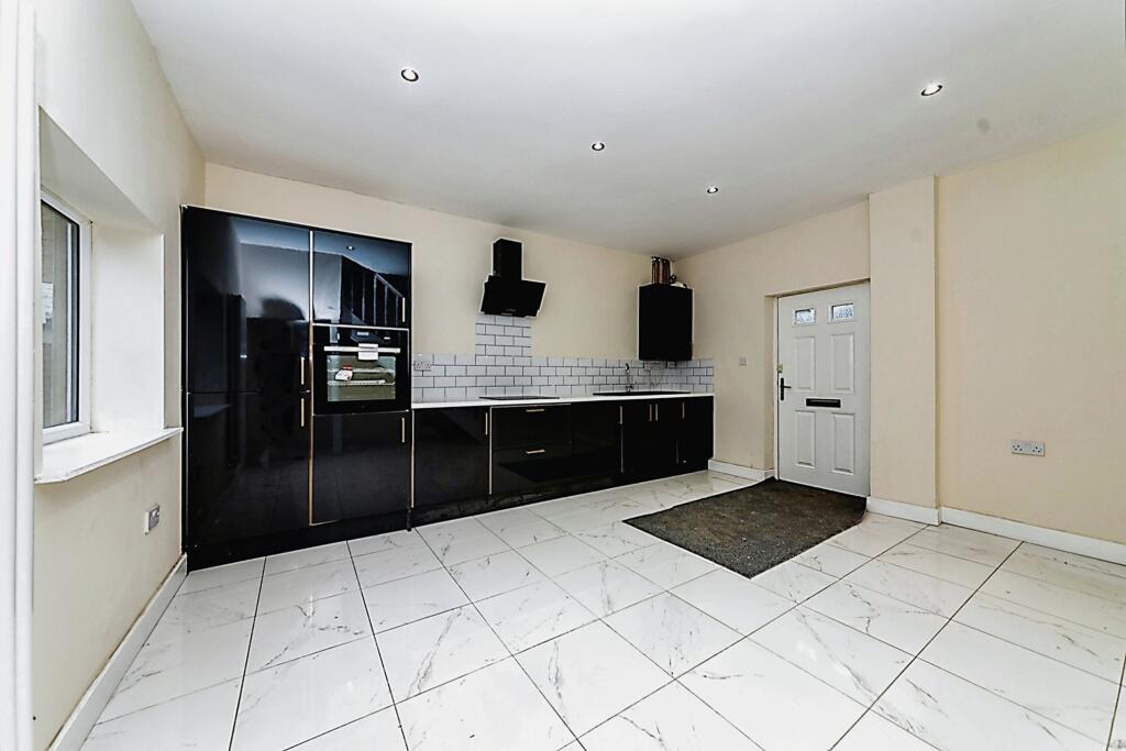 Property for sale by Auction A modern kitchen with glossy black cabinets, white countertops, grey backsplash tiles, and built-in appliances presents a substantial residential and development opportunity. The space features white tiled flooring, recessed lighting, a window on the left, and a door on the right leading to another room. Presented by Palace Auctions