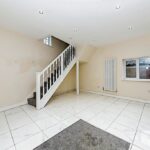 Property for sale by Auction A clean, modern room with white tiled floors and light-colored walls. A carpeted staircase with a white banister leads upwards. A single window is on the wall to the right, and a tall radiator stands beside it, creating a substantial residential and development opportunity. Recessed lighting fixtures are set in the ceiling.
 Presented by Palace Auctions
