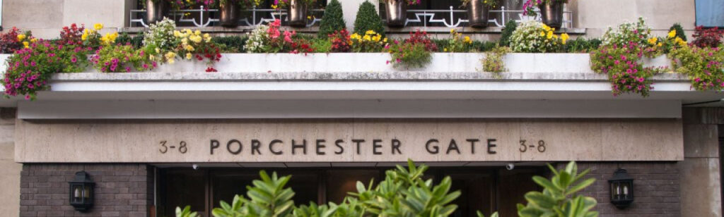 Property for sale by Auction Front entrance of Porchester Gate, a building marked with the address 3-8. The facade features a balcony adorned with various colorful flowers, with greenery visible in the foreground. Two black lantern-style lights are mounted on either side of the entrance. Presented by Palace Auctions