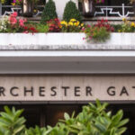 Property for sale by Auction Front entrance of Porchester Gate, a building marked with the address 3-8. The facade features a balcony adorned with various colorful flowers, with greenery visible in the foreground. Two black lantern-style lights are mounted on either side of the entrance. Presented by Palace Auctions