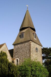 Property for sale by Auction A stone church tower with a steep, pointed roof and a weather vane on top. The tower has a clock face and is surrounded by greenery. The sky is clear and blue. Presented by Palace Auctions
