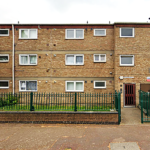 Property for sale by Auction The three-story brick apartment building at 94 Mortlake Road features uniform rectangular windows, bordered by a green metal fence. A small green yard is visible in front, with a sign near the entrance gate. The sky is overcast. Presented by Palace Auctions
