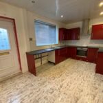 Property for sale by Auction A kitchen with red cabinets, a tiled floor, and white walls. It features an oven, stove, and a metallic sink under a large window. A door with a decorative glass panel is on the left. The room has modern lighting and a white painted ceiling. Presented by Palace Auctions