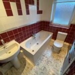 Property for sale by Auction A bathroom with a white sink, a bathtub, and a toilet. The walls are tiled with red and white tiles, and there's a frosted window. The floor has a light-colored wood pattern, and a metallic towel rack is mounted on the wall. Presented by Palace Auctions