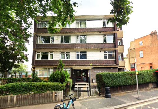 Property for sale by Auction A three-story apartment building with a brown and white exterior, surrounded by trees and shrubs. A blue bicycle is parked at the front near a bus stop, situated on a tree-lined street. Presented by Palace Auctions