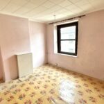 Property for sale by Auction An empty room with light pink walls, a single window with a black frame, and a small white radiator in the corner. The floor is covered with a yellow floral-patterned carpet, and a single bulb hangs from the ceiling. Presented by Palace Auctions