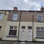 Property for sale by Auction A row of terraced houses with different colored facades under a cloudy sky. Each house has a distinct door and window design, some with satellite dishes and chimneys. The ground is paved with concrete. Presented by Palace Auctions